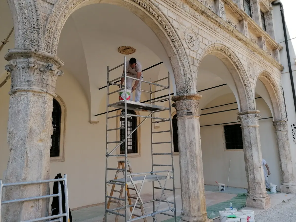 Imbianchino su un trabattello mentre dipinge il portico di un edificio storico, con pavimento protetto da teli
